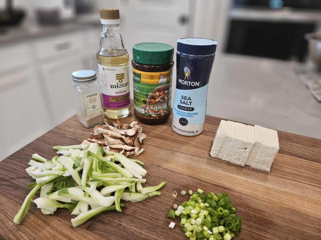 Chopped bok choy, green onions, salt, pepper, chicken powder, tofu, and mushrooms on cutting board