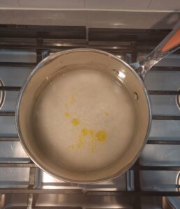 Water, rice, and oil in a stainless-steel pot on an oven burner
