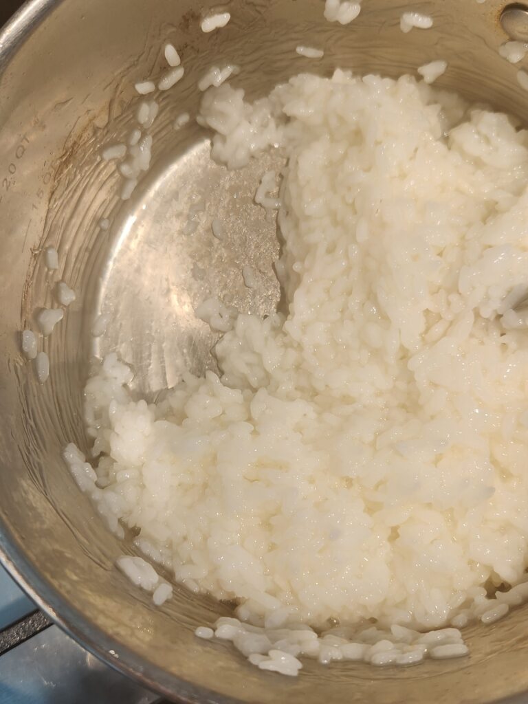 Picture of white rice in a stainless-steel pot that is very sticky and clumpy.  