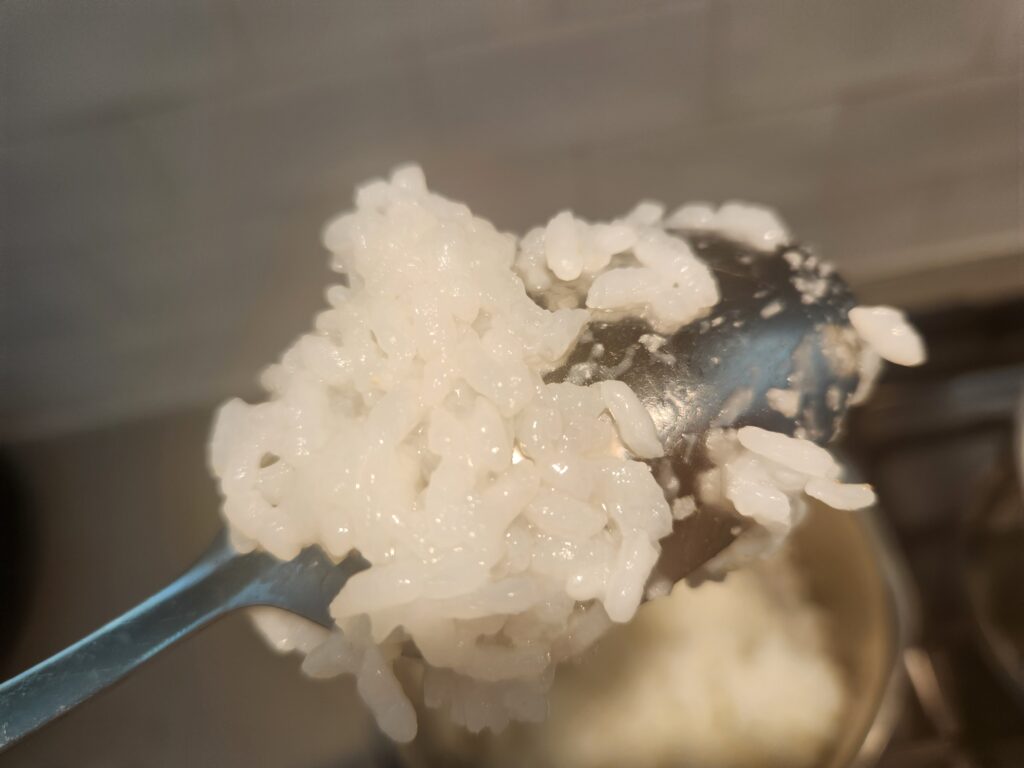 Picture of sliver spoon with very sticky, over-cooked white rice attached and clumped together. 