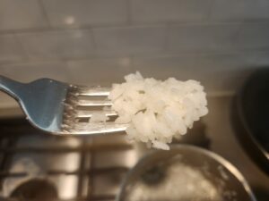 Cooked white rice shown on the tip of a fork. The rice is not too sticky or dry. It is light and fluffy.