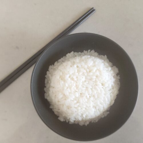 white rice in a black bowl with black chop sticks nearby